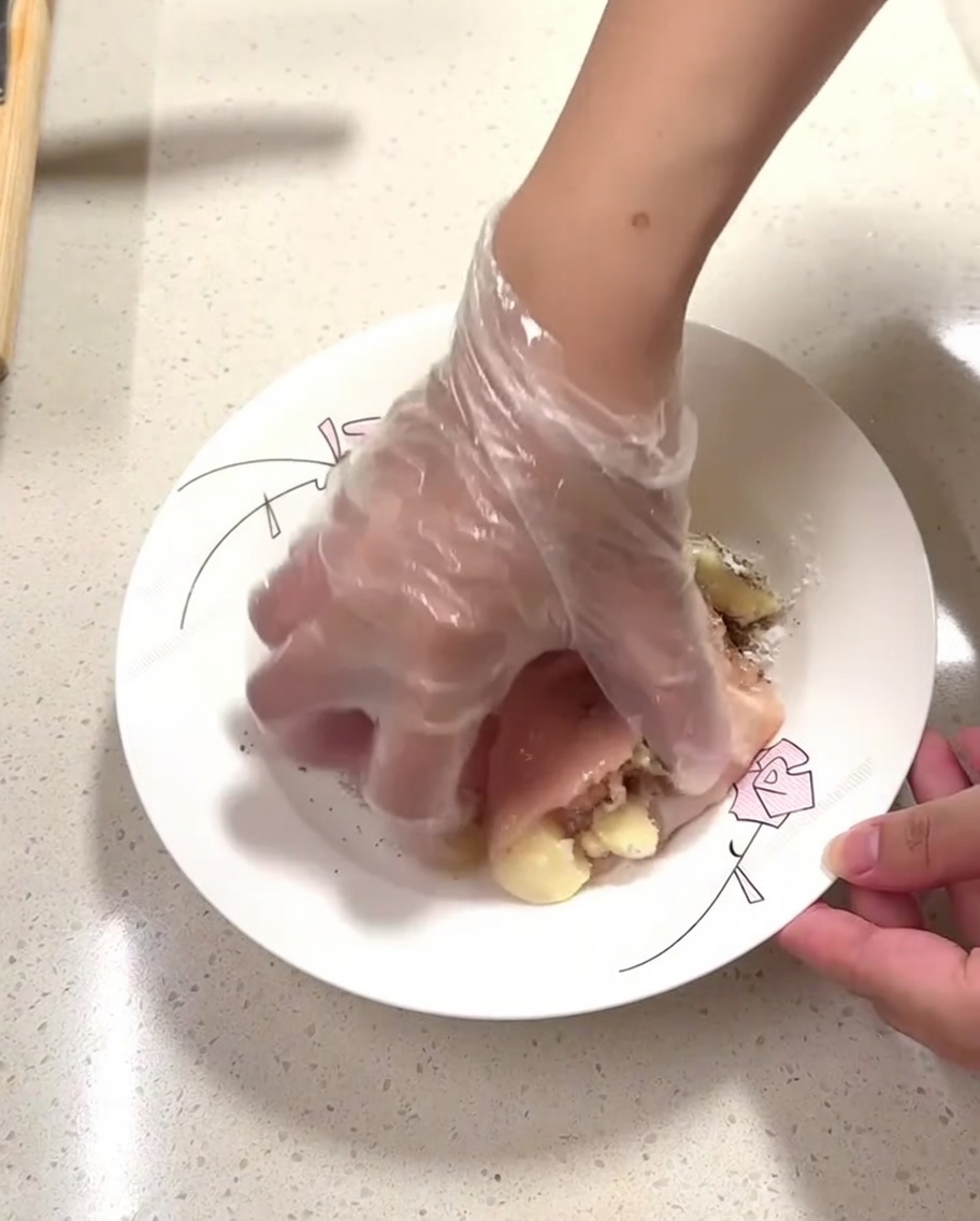手袋をした手で、皿の上の鶏肉に調味料を揉み込んでいる様子。
