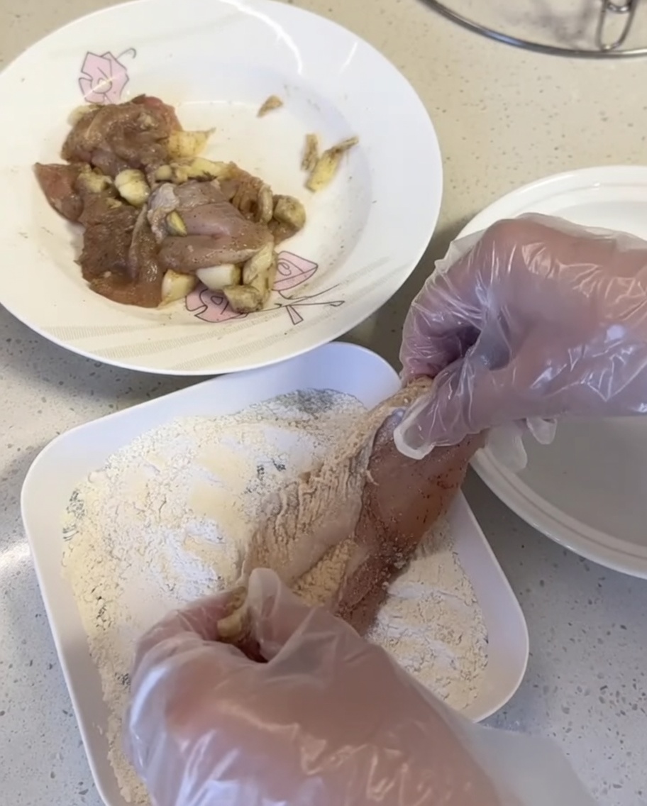 白い皿の上で、鶏肉にパン粉ミックスを押し付けている様子。