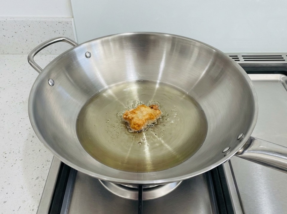 熱した油を入れた中華鍋で、衣を付けたチキンを揚げている様子。
