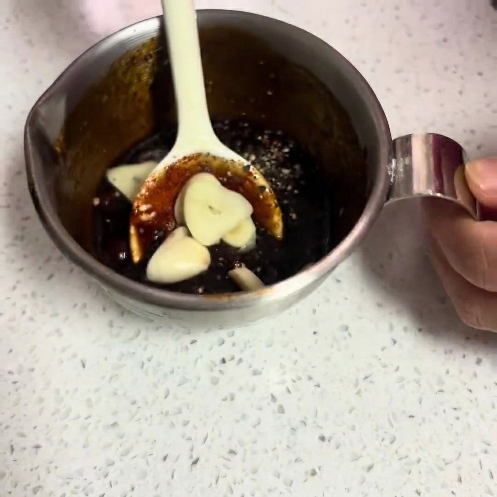 生のにんにくスライスが入った、とろみのある濃い色の漬けだれを混ぜている様子。
