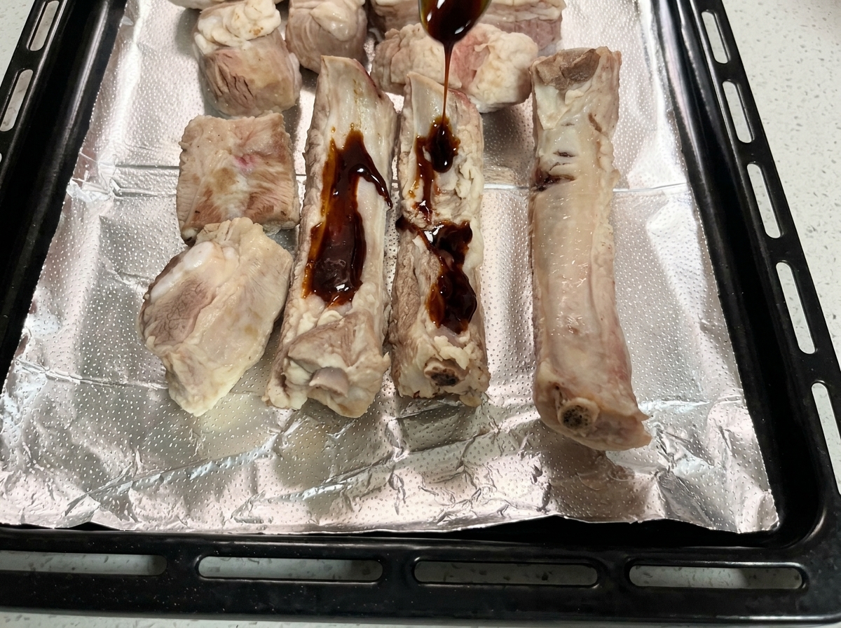 アルミホイルを敷いた天板の上で、豚肉にスプーンで濃い色の漬けだれをかけている様子。