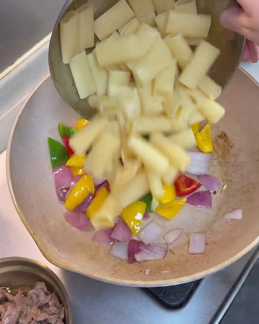 野菜が入ったフライパンに茹でたパスタを加えている様子。