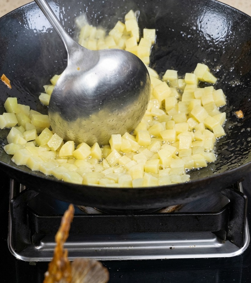 角切りにしたじゃがいもを、軽く焼き色がつくまで中華鍋で炒めている様子。