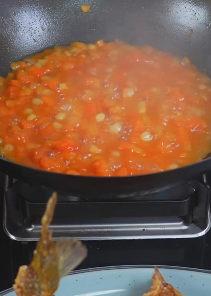 炒めたじゃがいもとトマトが入った中華鍋に、沸騰したお湯を注いでいる様子。