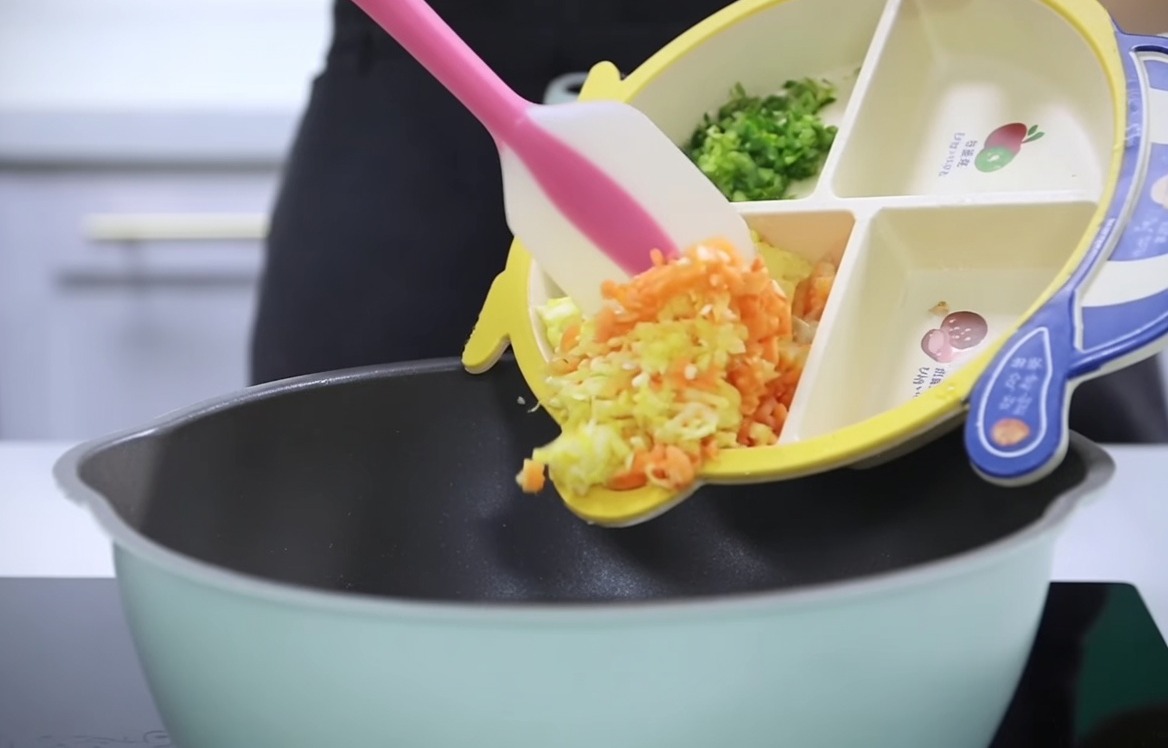 細かく刻んだにんじん、じゃがいも、セロリを、仕切り付きのベビー用プレートから鍋に移している様子。