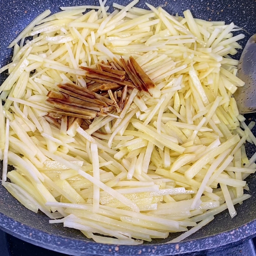 炒めたじゃがいもに醤油とオイスターソースを加えている様子。