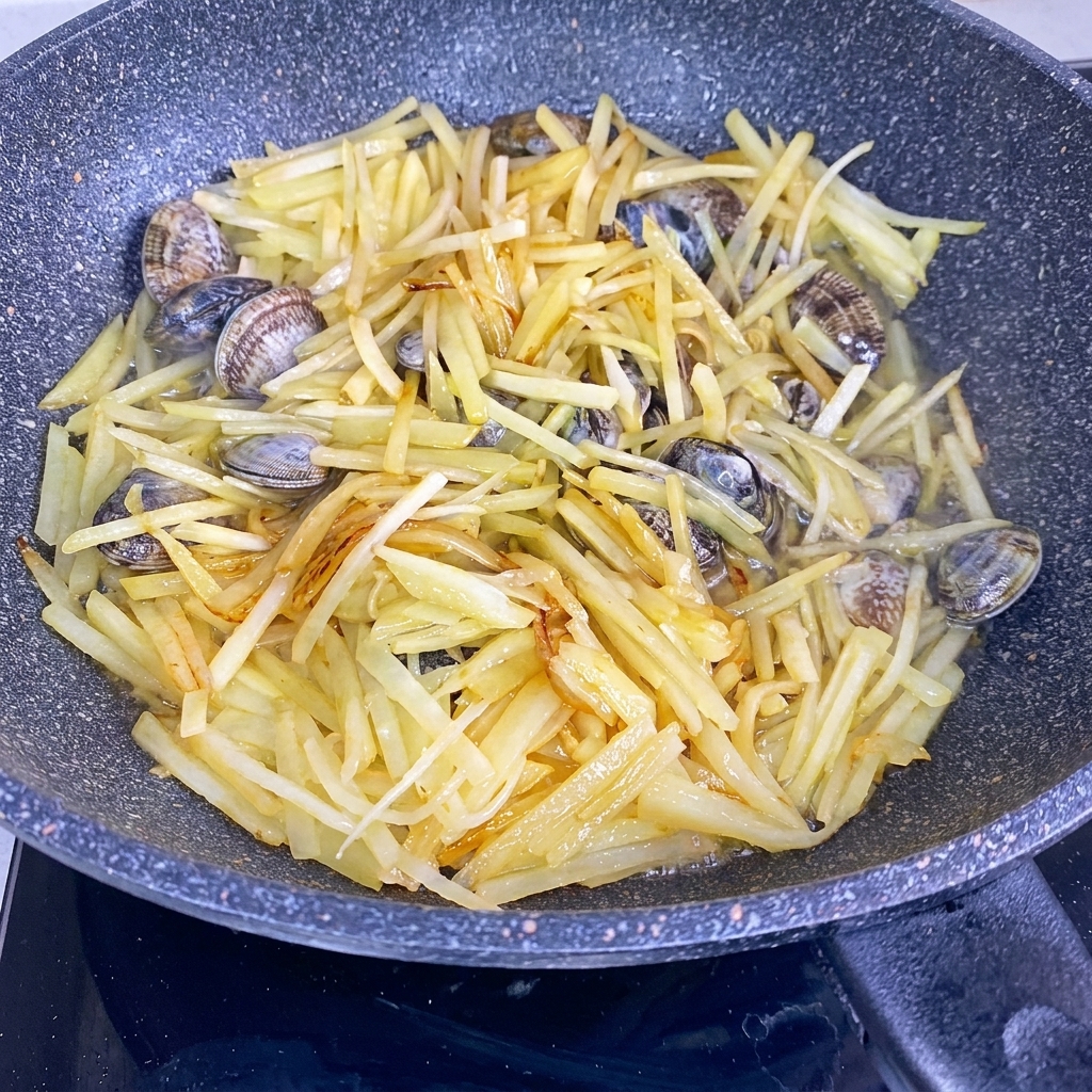 水が注がれた鍋で煮込まれているじゃがいもとあさり。
