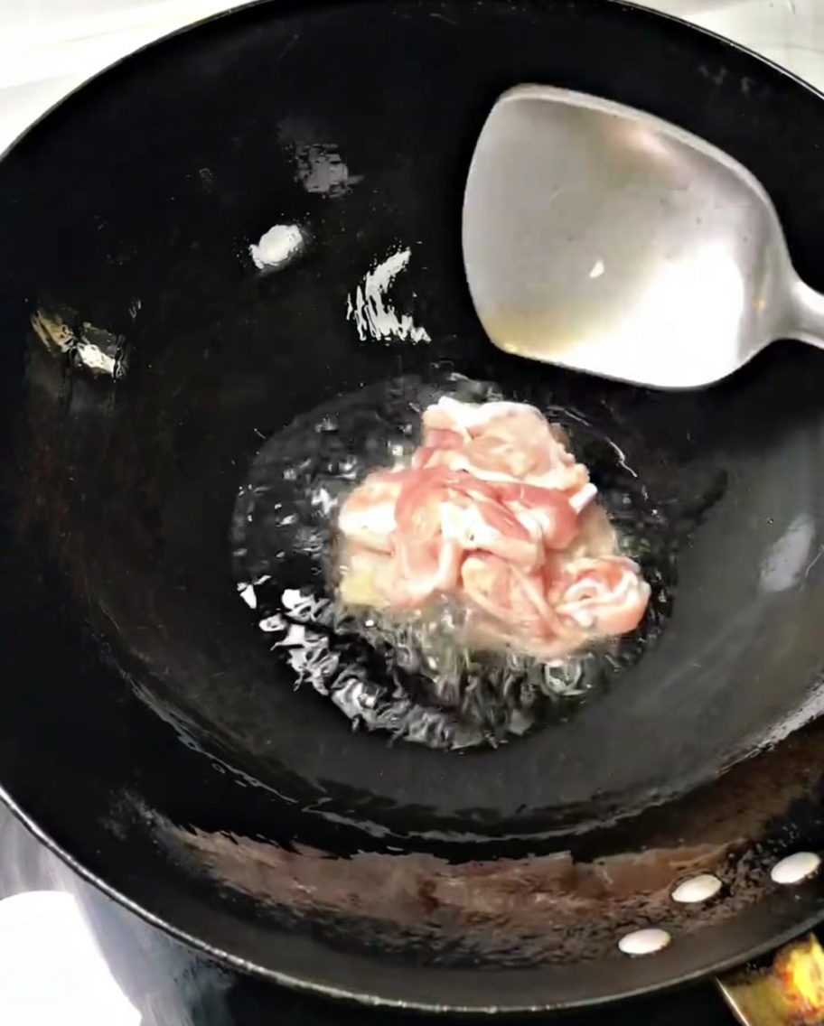 熱した中華鍋に油を引き、スライスした豚肉を金属製のヘラで炒めている様子。