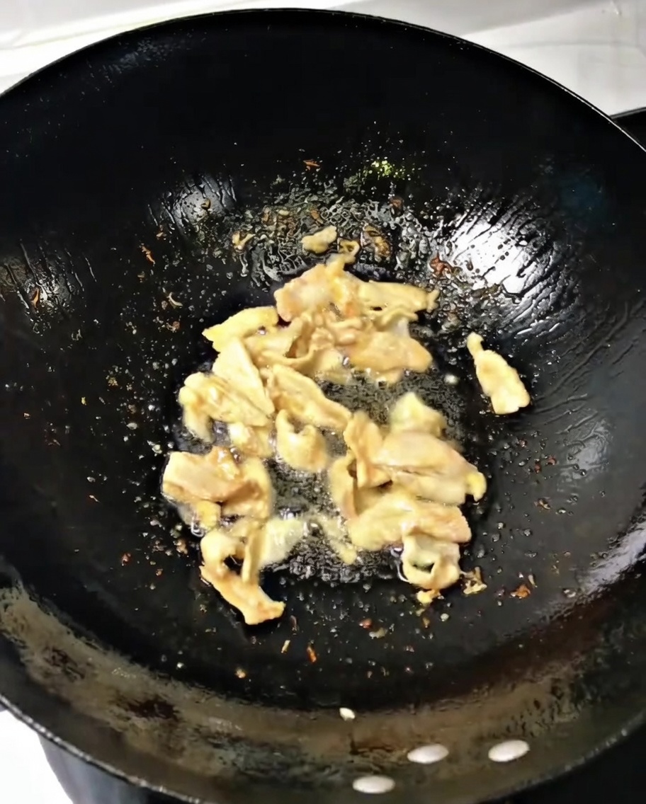 炒めた豚肉に刻んだ長ねぎと生姜を加え、中華鍋で混ぜ合わせている様子。