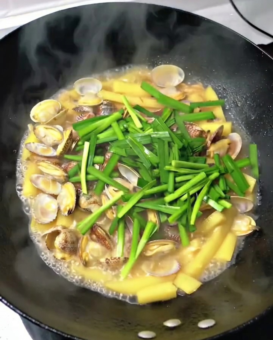 出来上がったあさりとジャガイモの炒め物に、刻んだニラを散らしている様子。