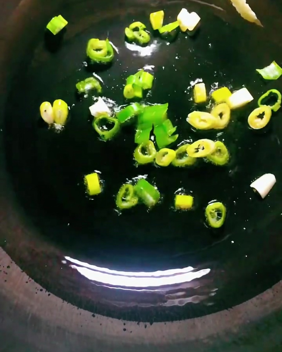 黒い中華鍋の熱い油で青ねぎを炒めている様子。