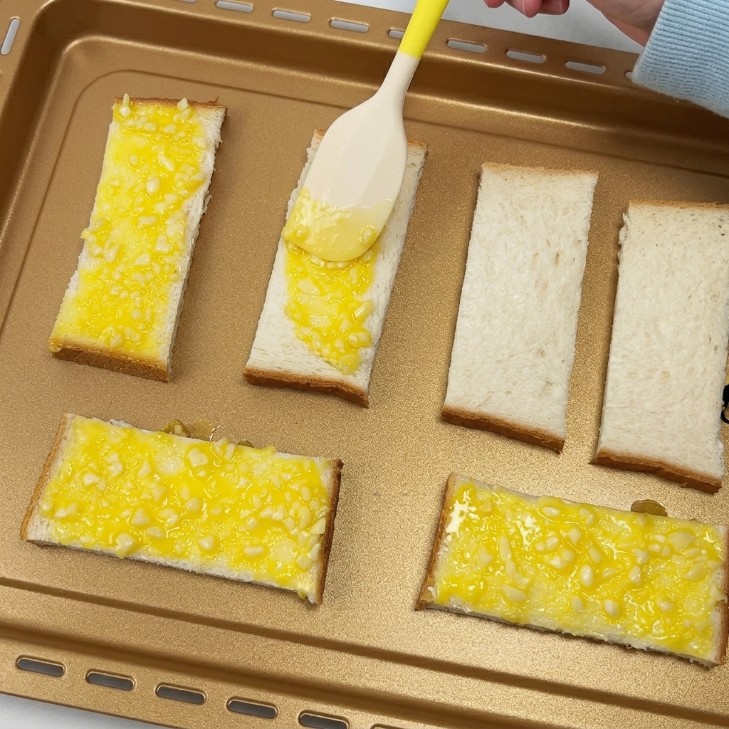 天板に並べたパンに、スパチュラでガーリックバターを塗っている様子。