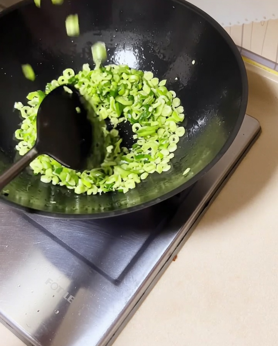 炒めた青ねぎの入った中華鍋に、刻んだいんげん豆を入れて混ぜ合わせている様子。