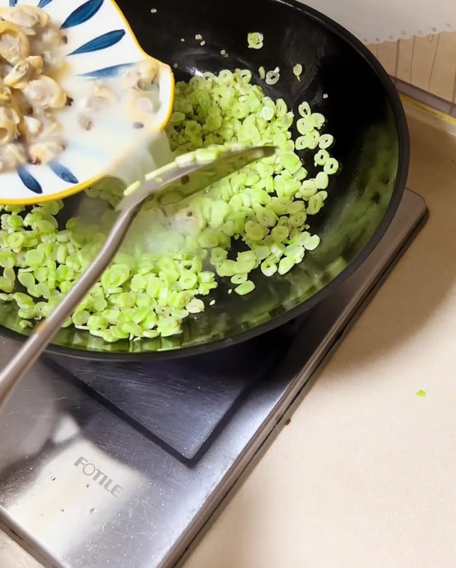 あさりの身とゆで汁を、いんげん豆の入った中華鍋に注ぎ入れている様子。