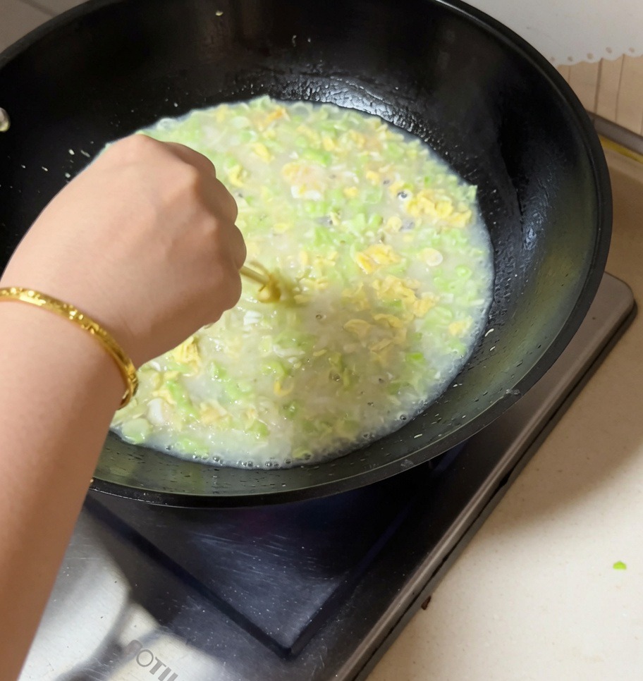 あさり、いんげん豆、卵のスープが入った中華鍋を箸で混ぜている手元の様子。