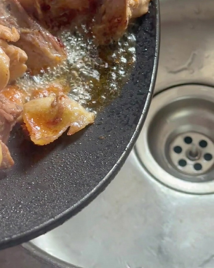 中華鍋を傾け、溶け出した鶏肉の脂を捨てる様子。