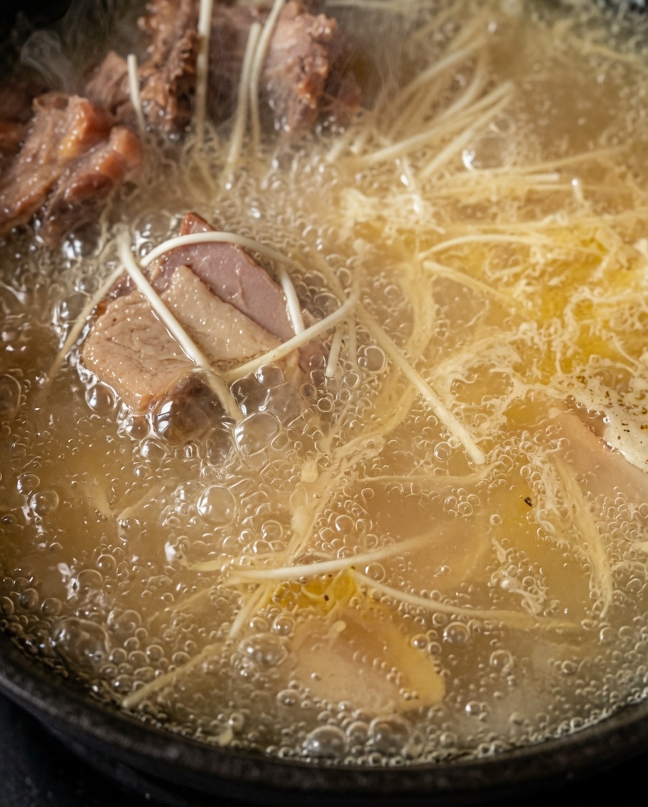 グツグツと煮立つ濃厚な白いチキンスープの中で麺が茹でられている様子。