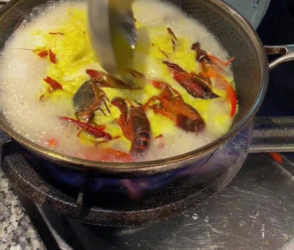 熱いザリガニのスープに、濃縮チキンブイヨンをお玉で混ぜ合わせている様子。