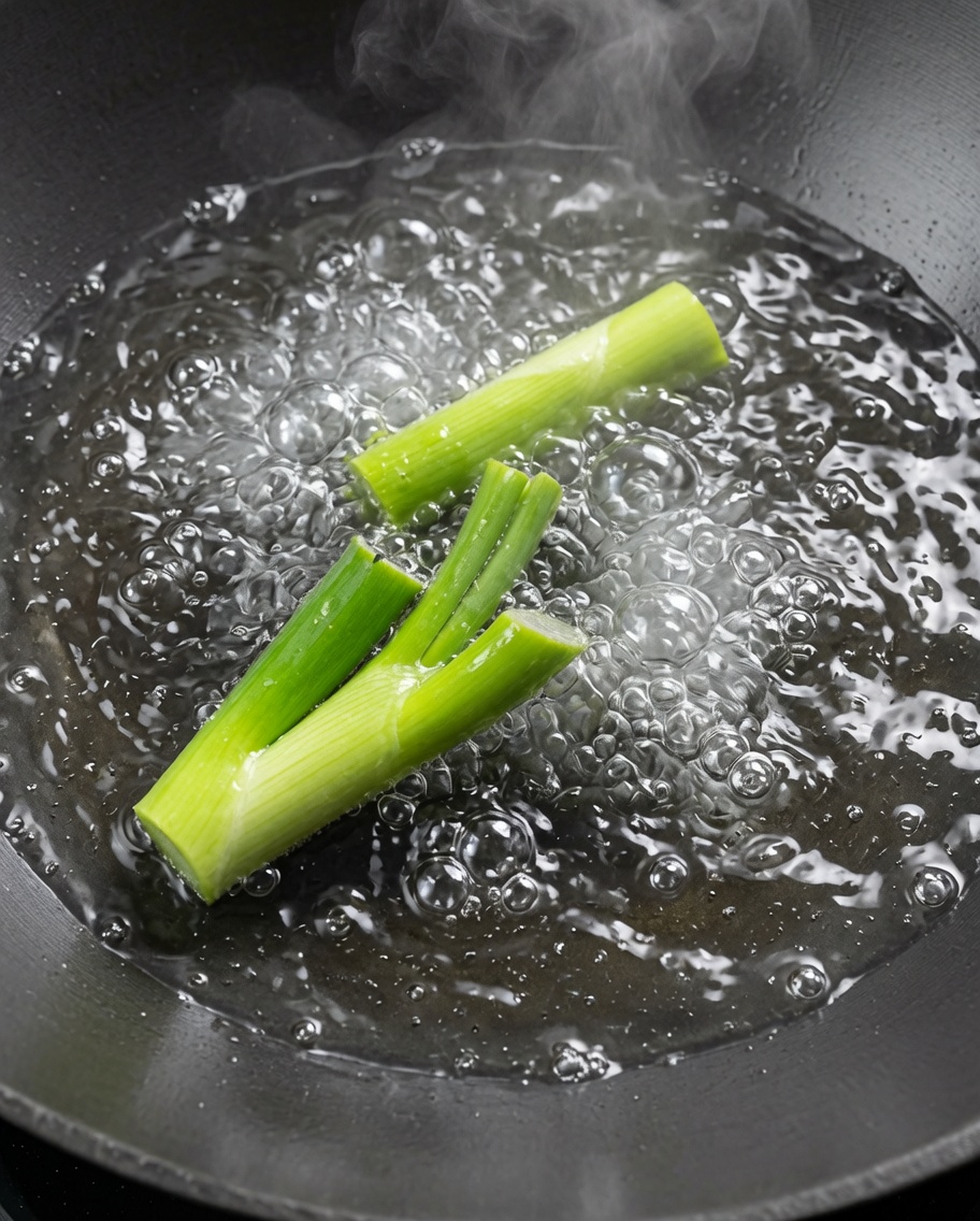 大きなお湯を沸かした中華鍋で、長ねぎと一緒にザリガニをサッと茹でている様子。