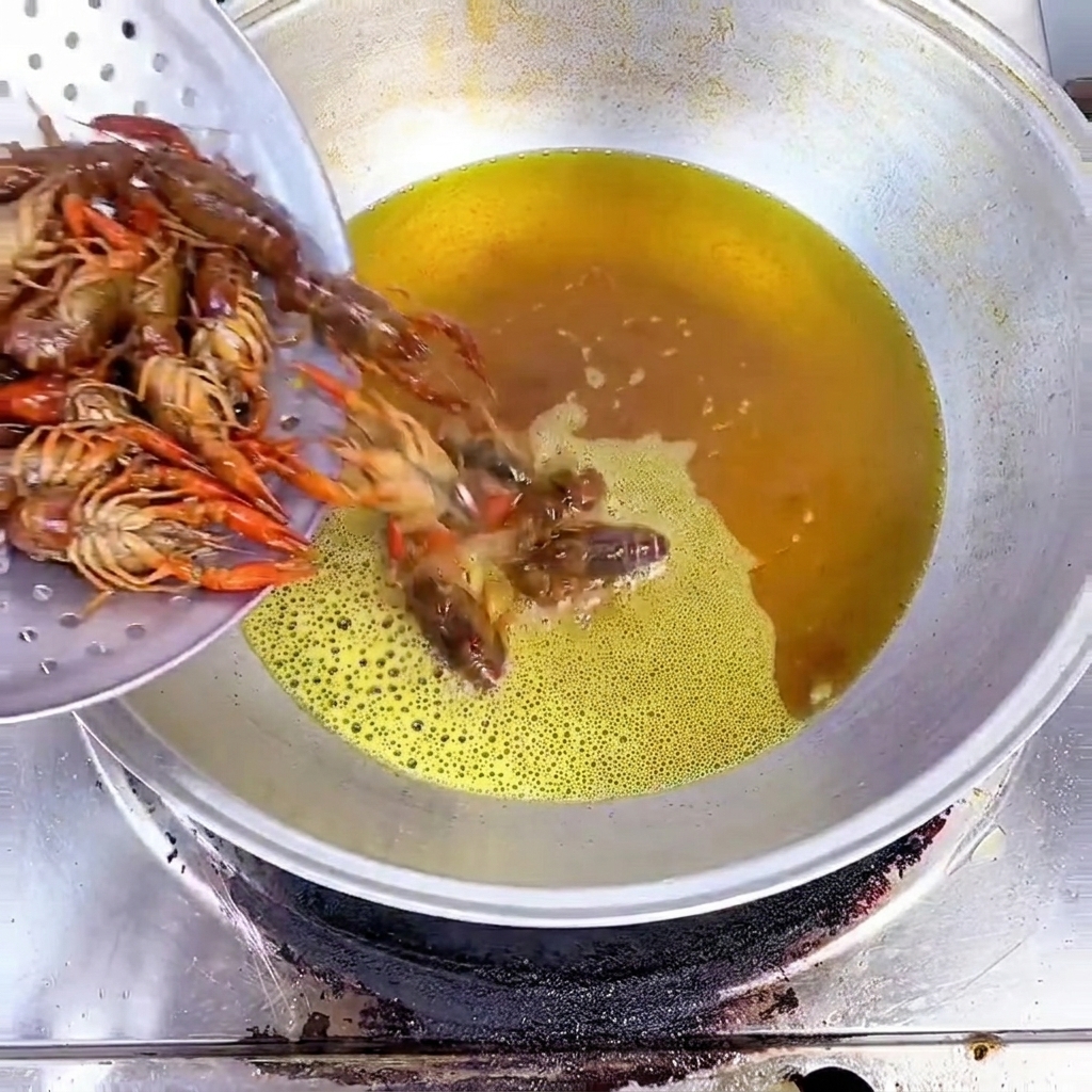 金属製のストレーナーから、熱した黄色の油が入った中華鍋に生のザリガニを入れる様子。