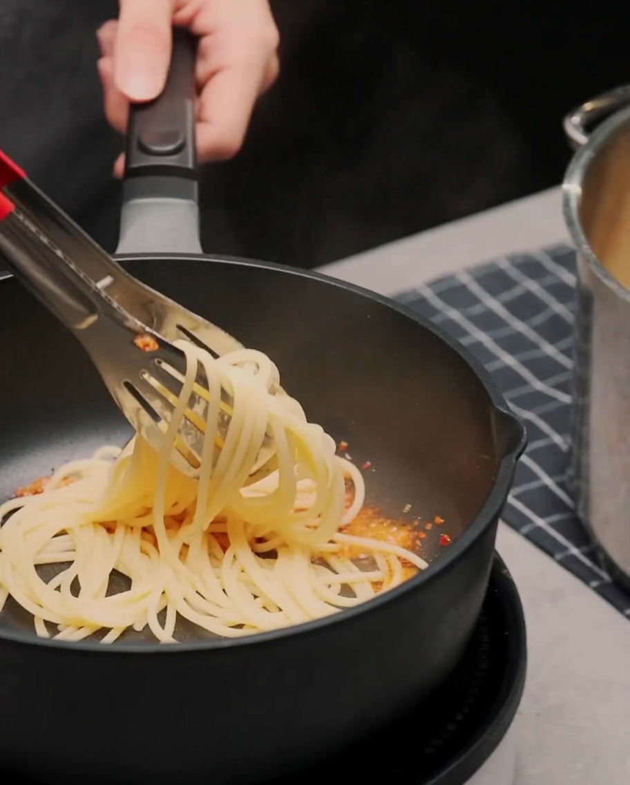 フライパンで茹で上がったスパゲッティをトングで混ぜ合わせている様子