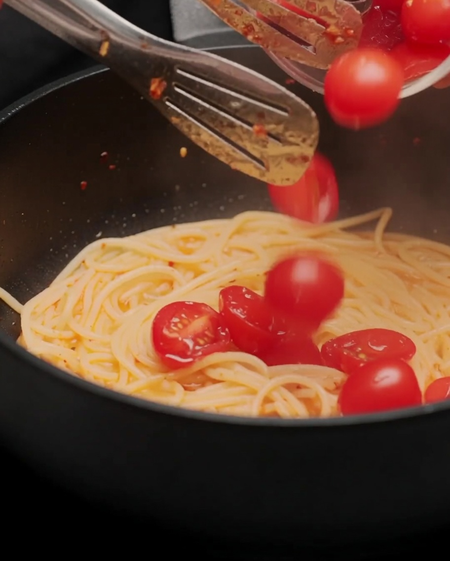半分に切ったトマトをフライパンに入れ、パスタと和えている様子