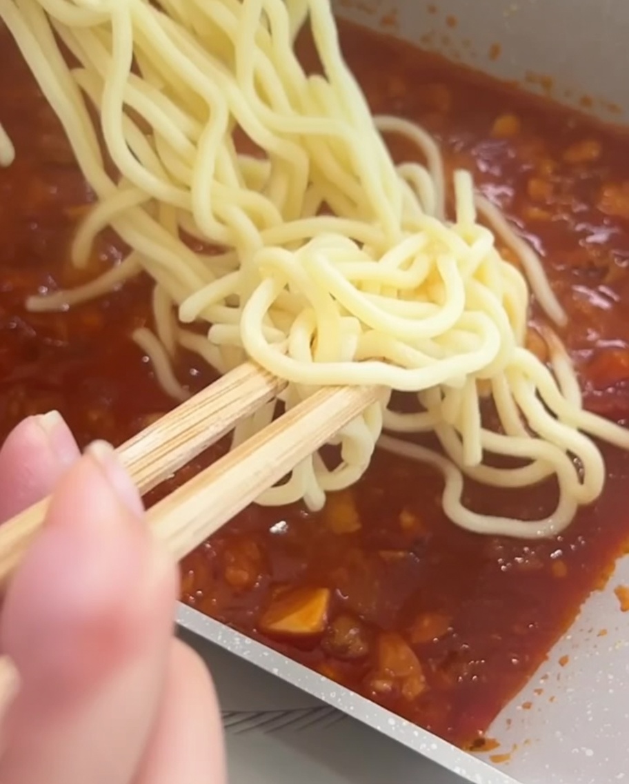 茹で上がったスパゲッティをフライパンに入れ、箸でソースと絡めている様子。