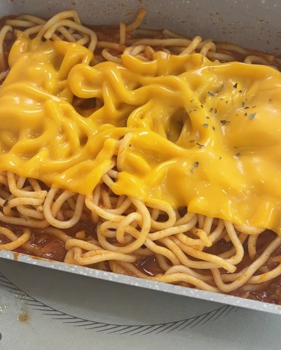 チーズがとろけたスパゲッティに、彩りのパセリが散らされている様子。