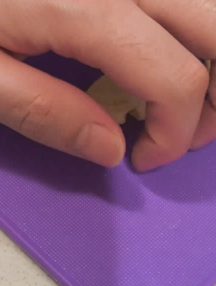 紫色のまな板の上で、包丁の腹を使ってにんにくを押し潰している様子。