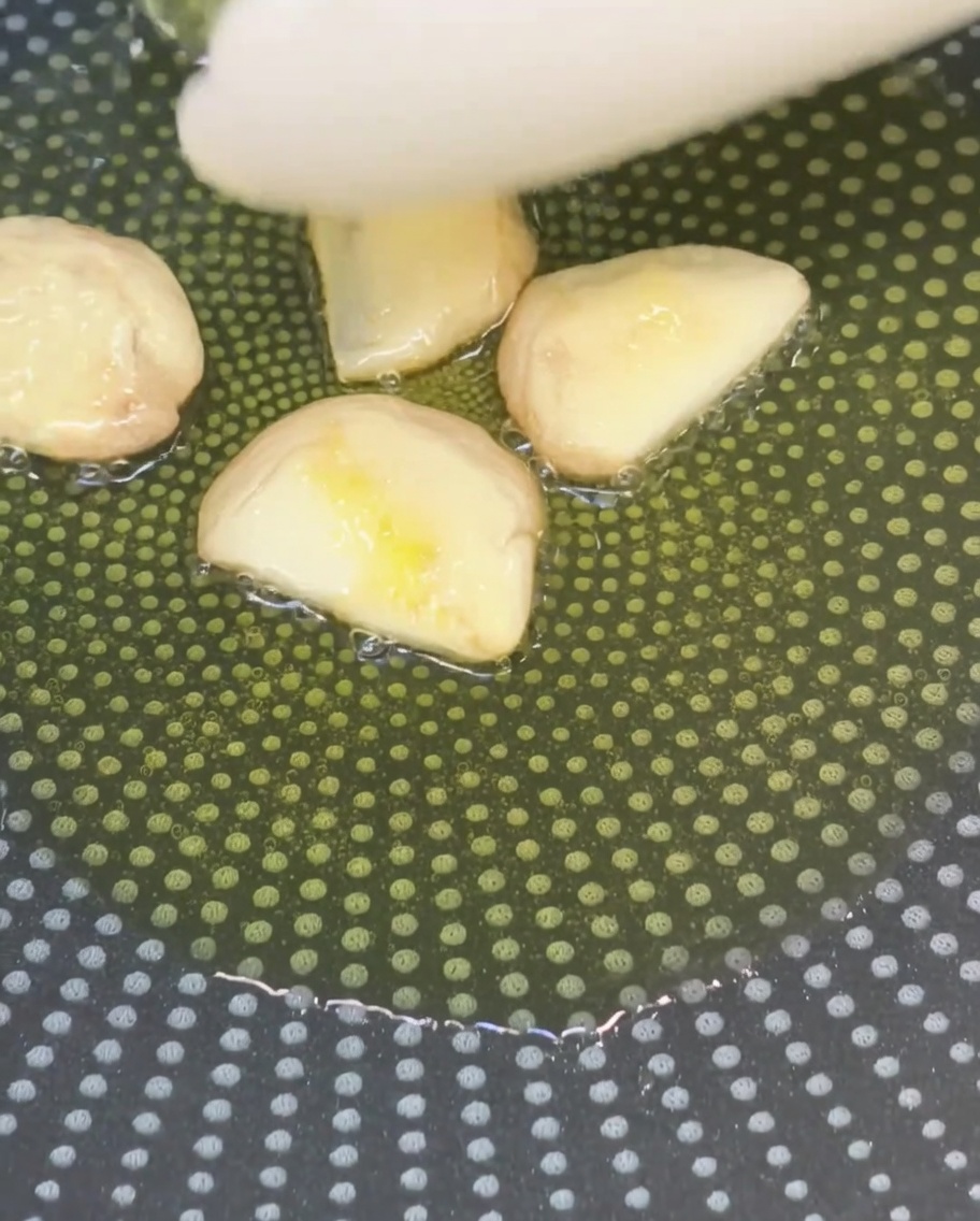 フッ素樹脂加工のフライパンで、潰したにんにくをオリーブオイルで炒めている様子。