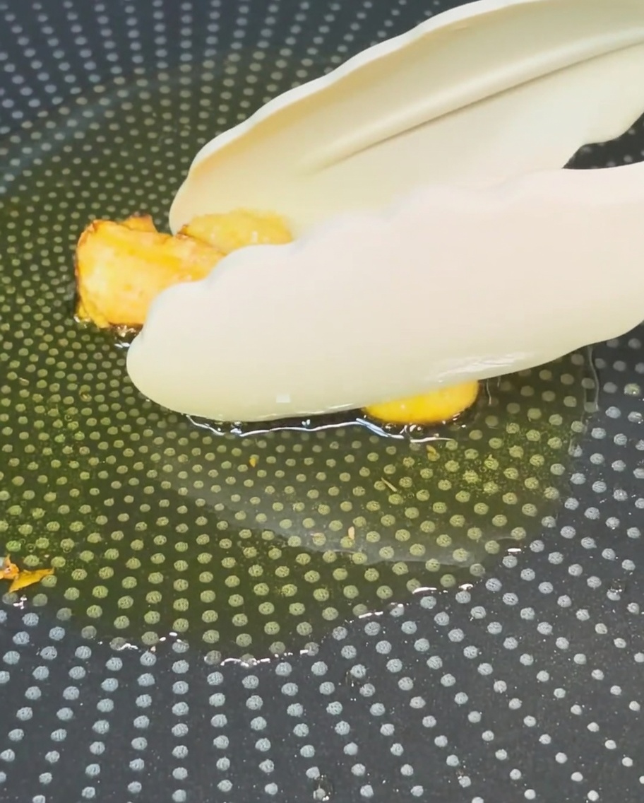 きつね色に揚がったにんにくを、トングでフライパンから取り出している様子。