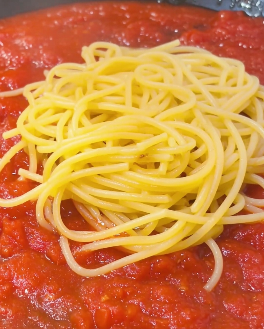 パスタとトマトソースが入ったフライパンに、でんぷん質の茹で汁をお玉ですくい入れている様子。