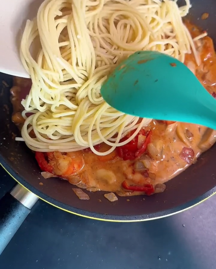 茹で上がったスパゲッティをソースに入れて、緑色のスパチュラで和えている様子