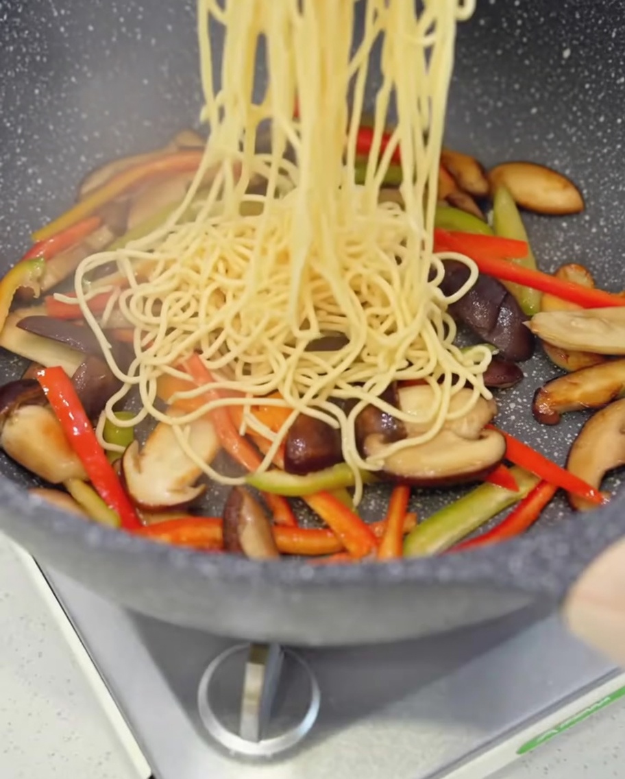 炒めたキノコと野菜の中にスパゲッティを加えている様子。