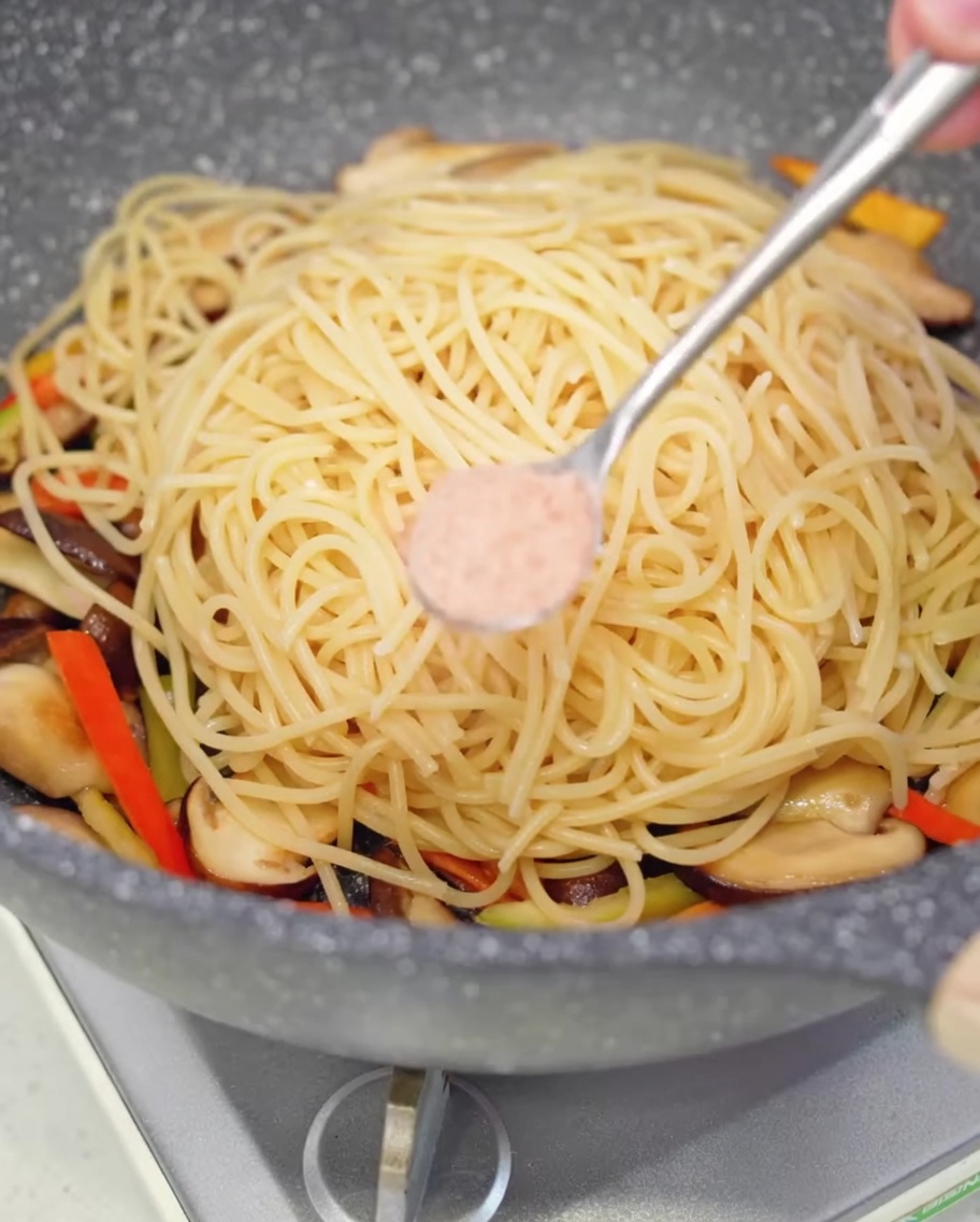 フライパンの中のパスタに少量の塩を振りかけている様子。