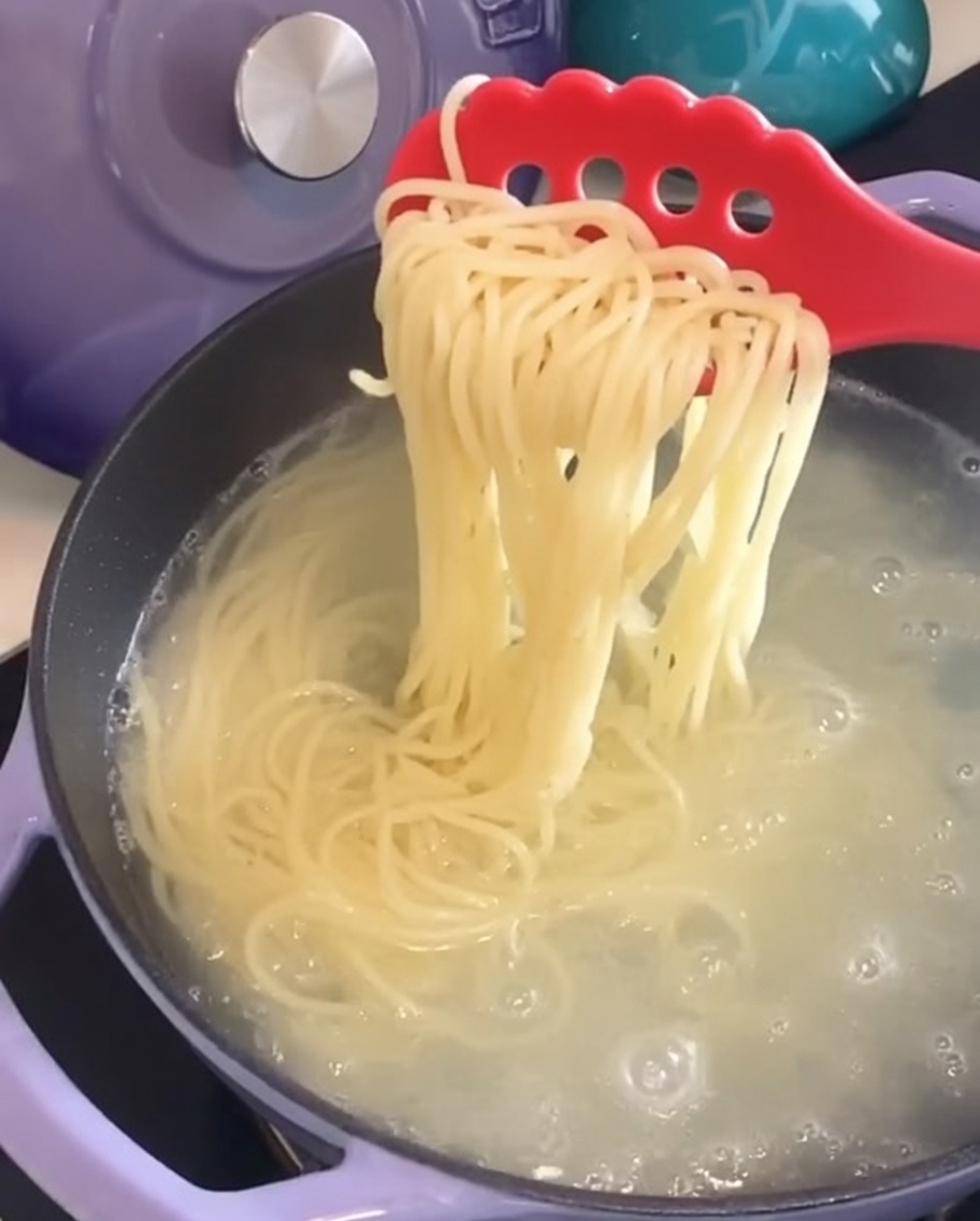 赤いパスタフォークを使って、鍋からすくい上げられている茹で上がったスパゲッティ。