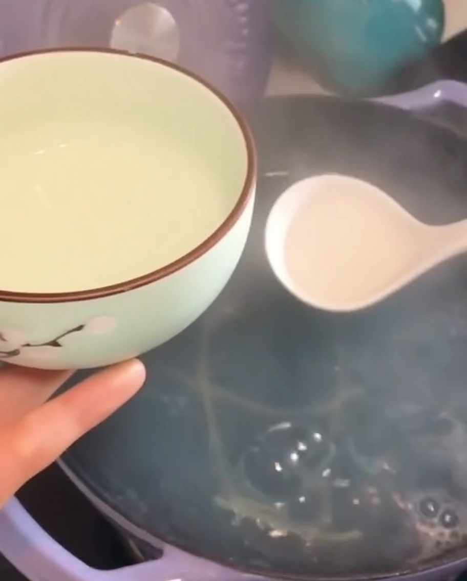 白いお玉で、湯気の立つパスタの茹で汁を小さな器にすくっている様子。