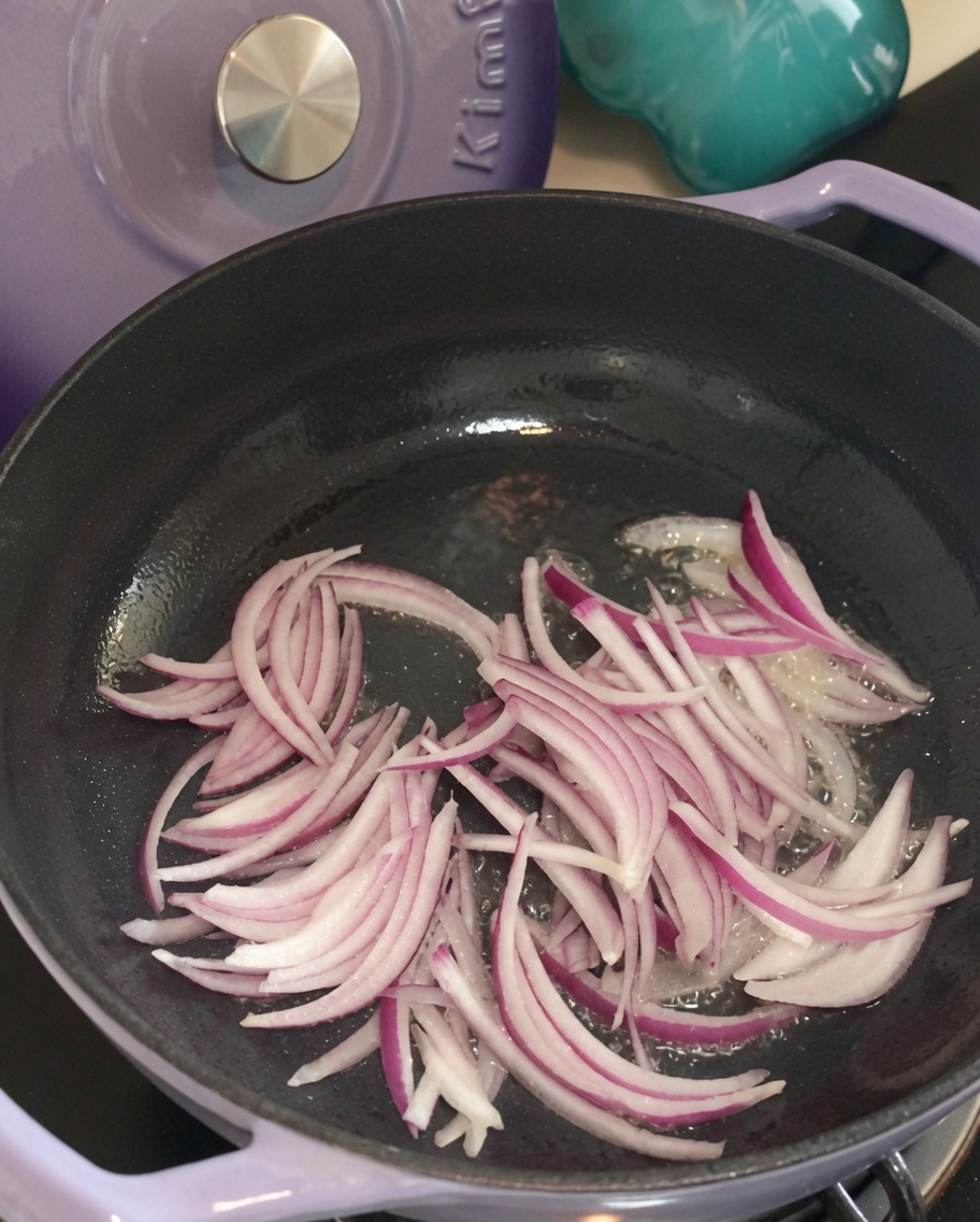 熱したフライパンで炒められ、しんなりしてきた紫玉ねぎのスライス。