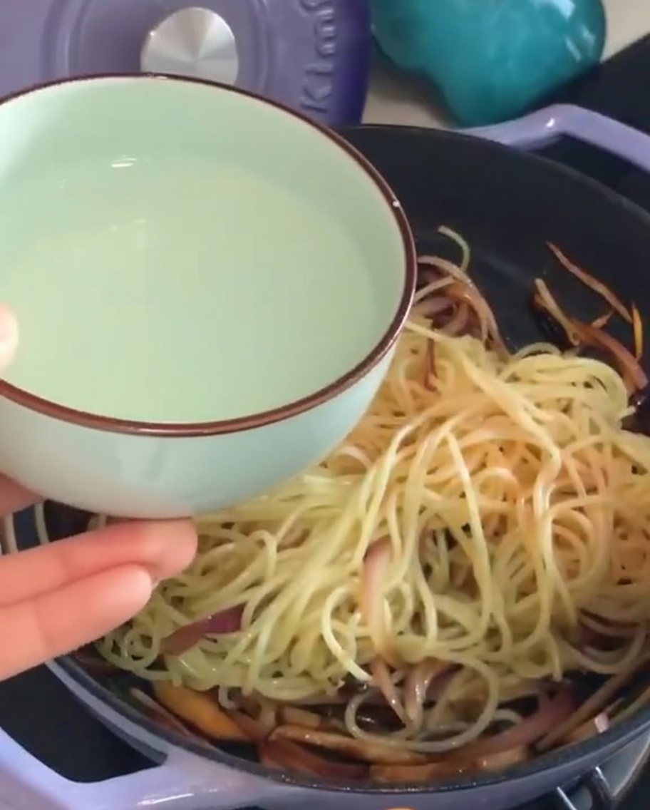 スパゲッティと具材の入ったフライパンに、取り分けておいた茹で汁を注いでいる様子。