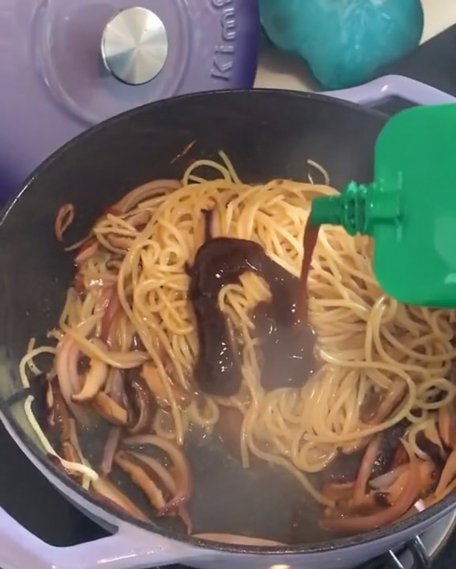 炒めたパスタの上に、緑色のパッケージからブラックペッパーソースを絞り出している様子。