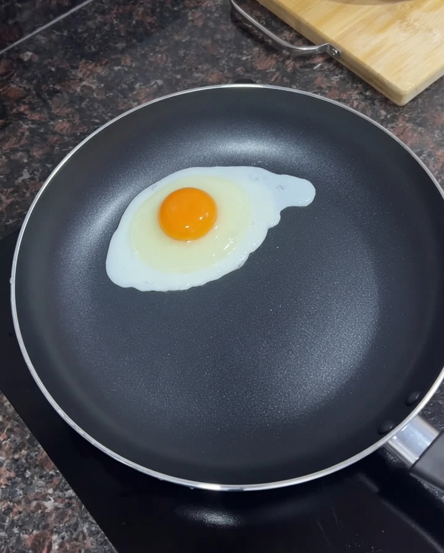 溶かしたバターを入れた黒いフライパンで目玉焼きを作っている様子。