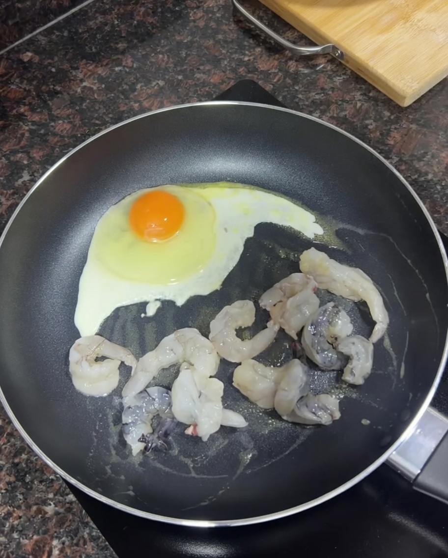 フライパンで卵の横で生のむきエビに焼き色をつけている様子。