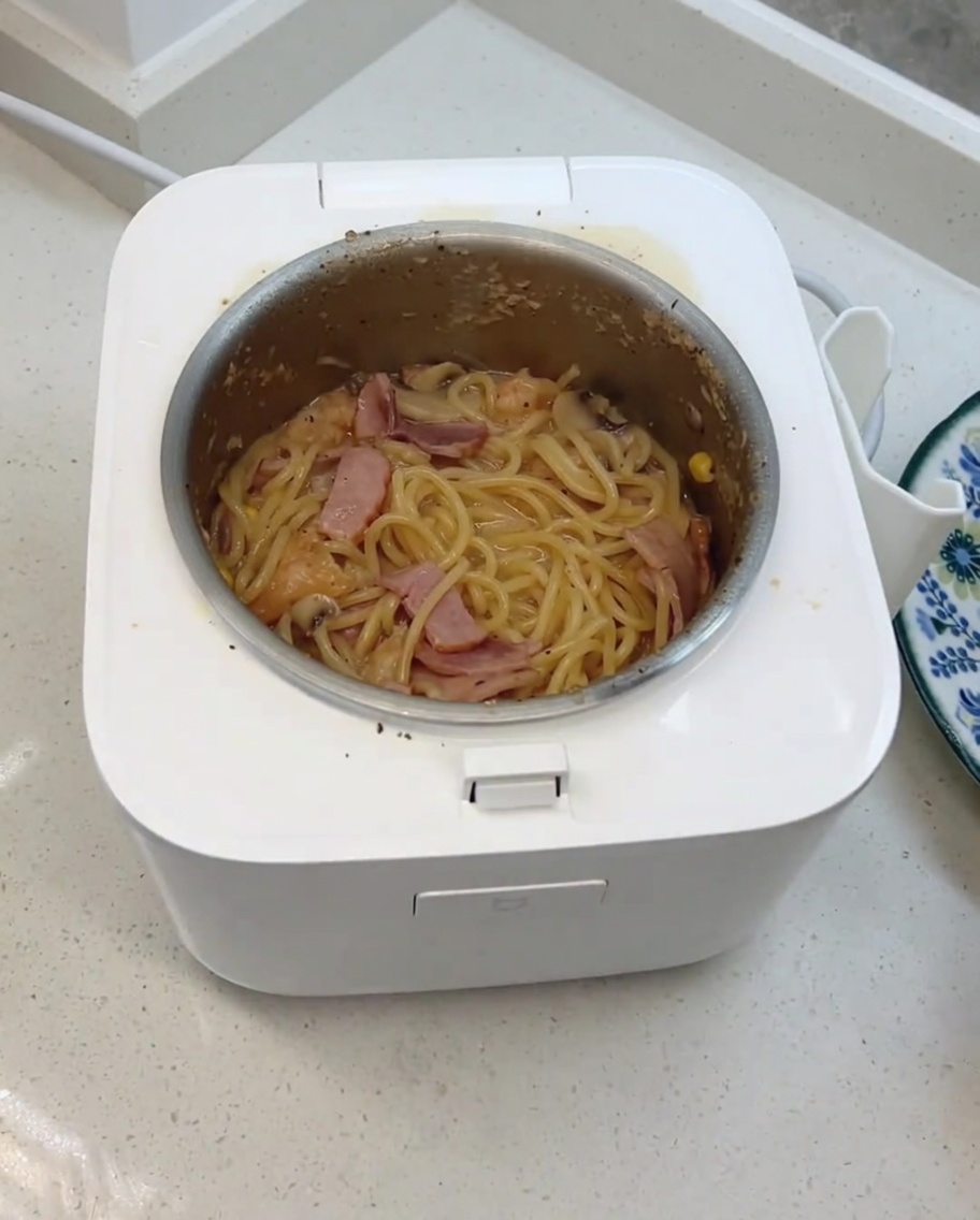 炊き上がったスパゲッティにチーズを加え、炊飯器の中でかき混ぜている様子。