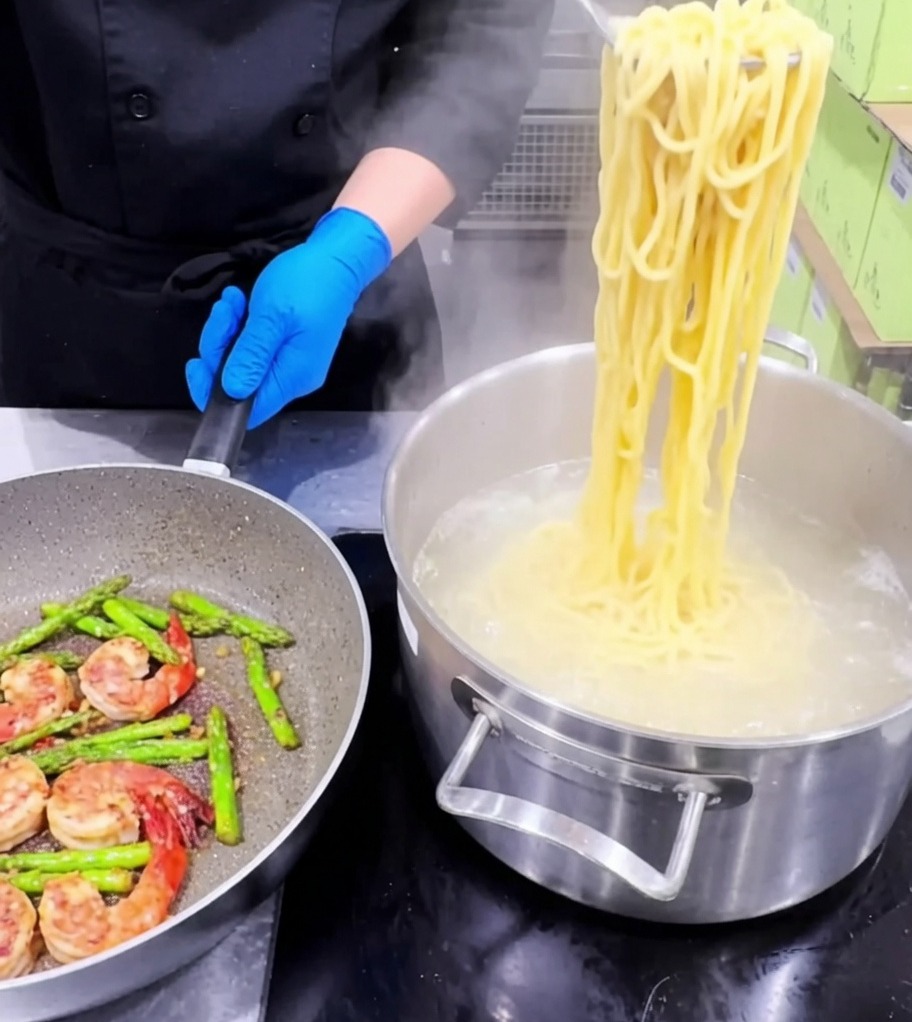 茹で上がったパスタをフライパンに加え、具材と混ぜ合わせている様子。