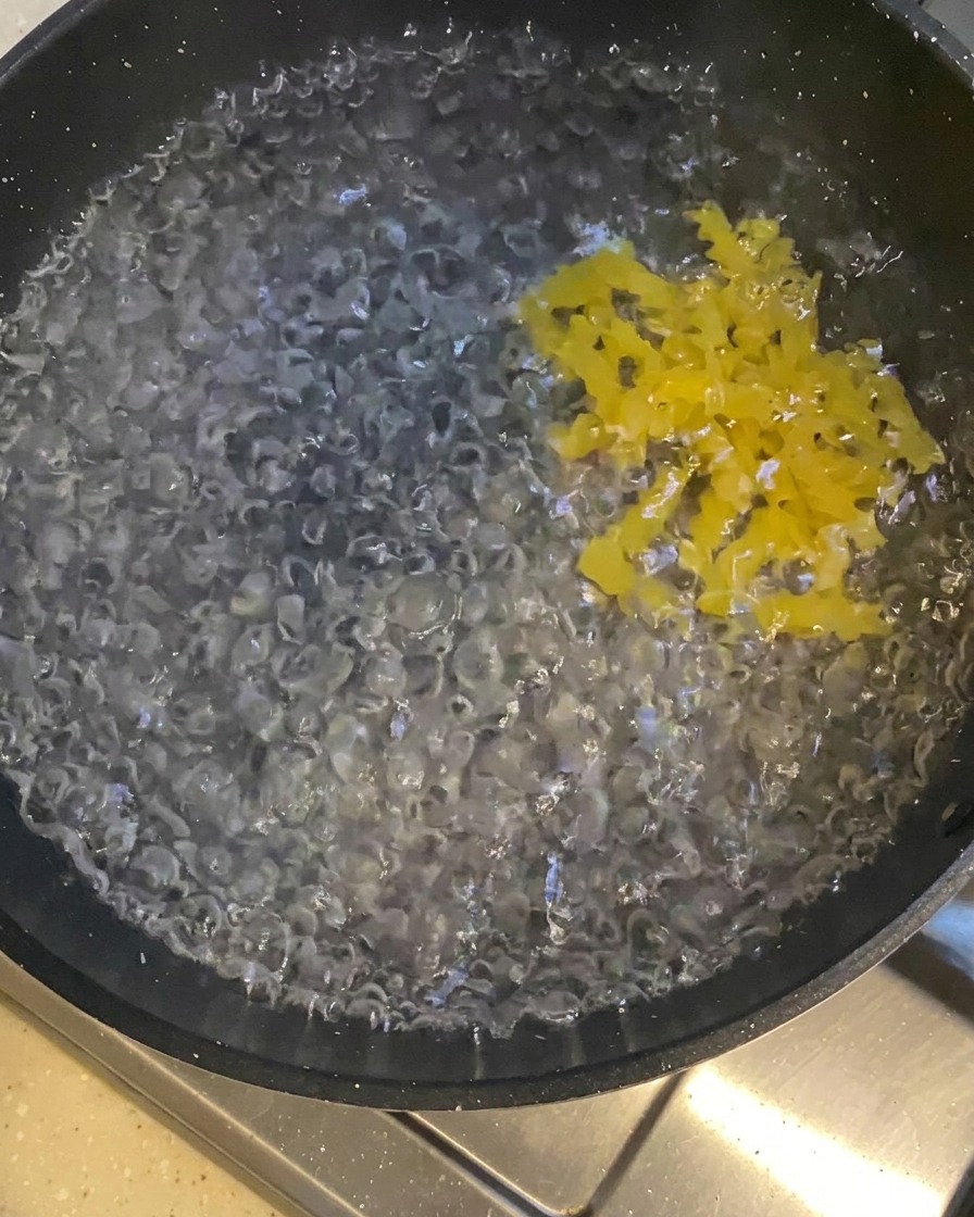 ぐらぐらと沸騰した鍋に、黄色いカール状のパスタが入っていく様子。