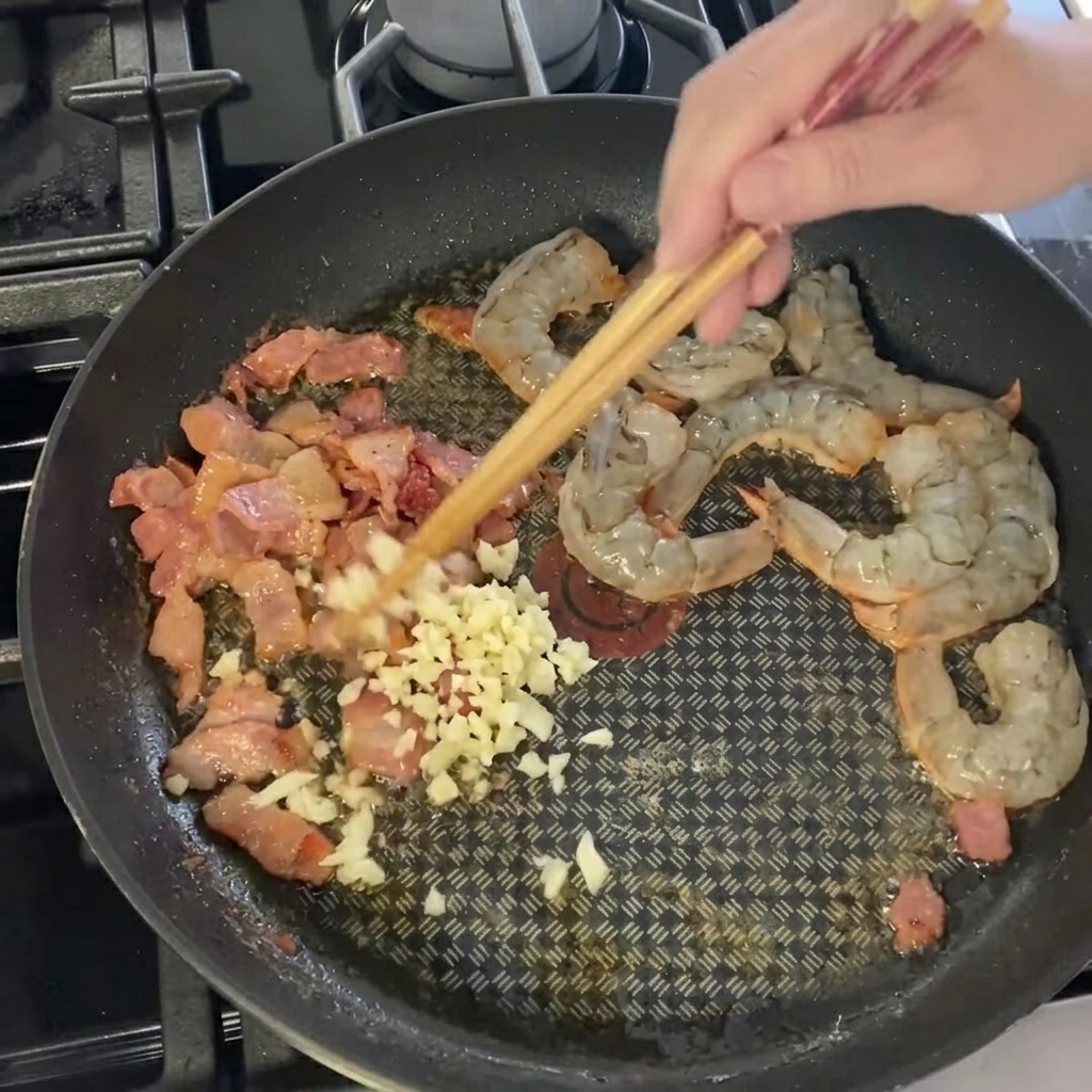 フライパンの具材にみじん切りニンニクを加える様子。