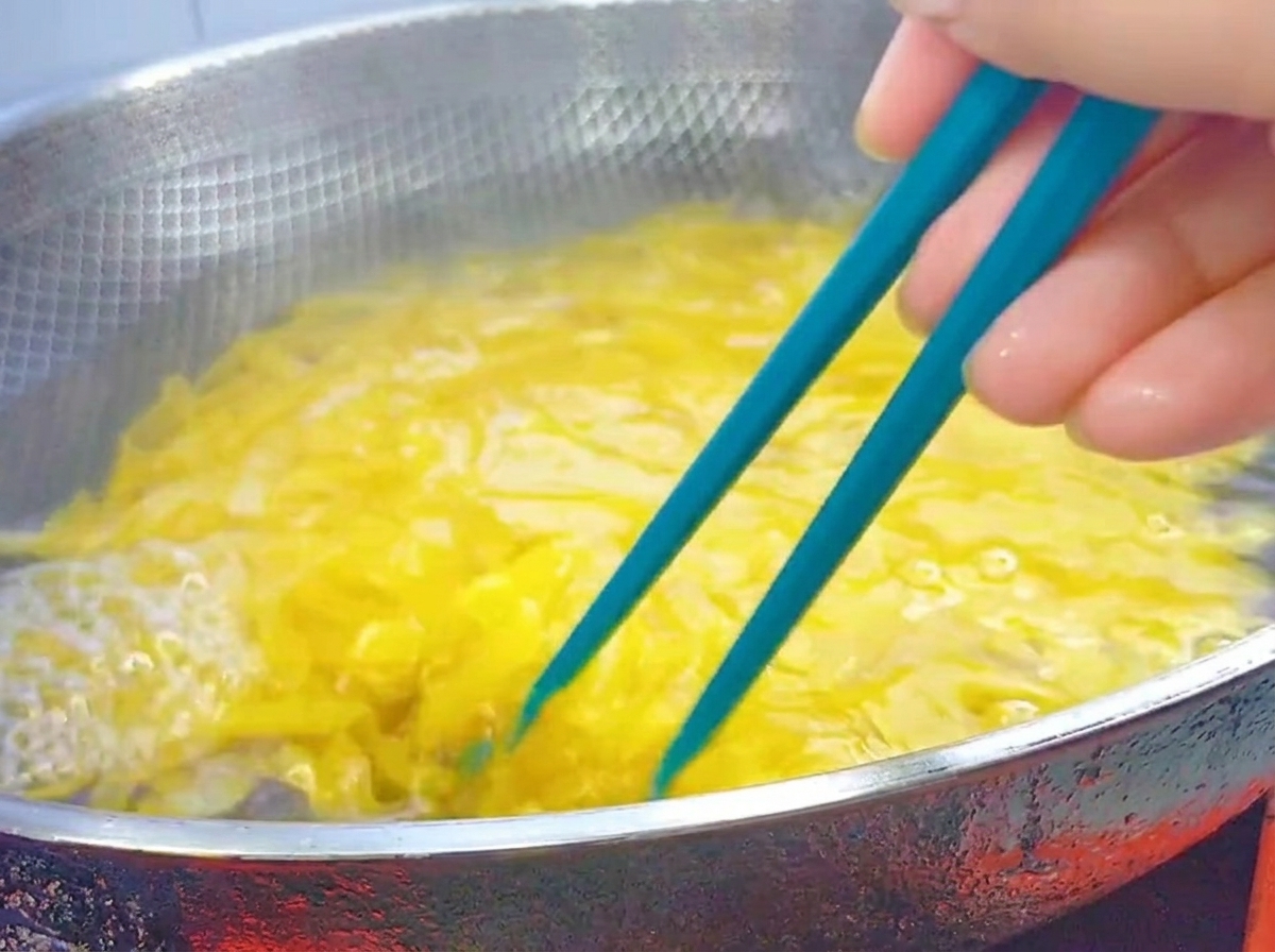 大きめの鍋で茹でているペンネを青い菜箸でかき混ぜている様子。
