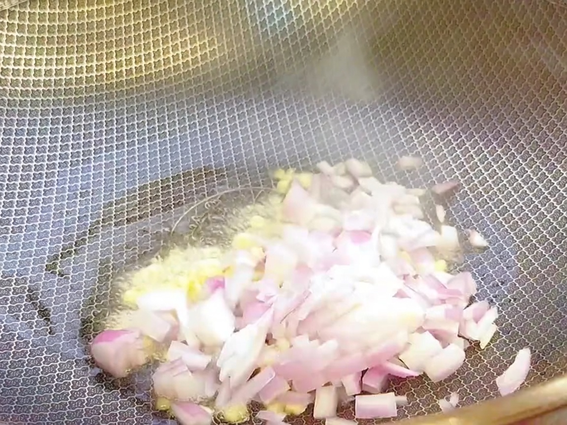 熱したフライパンに油をひき、みじん切りにしたにんにくと玉ねぎを炒めている様子。