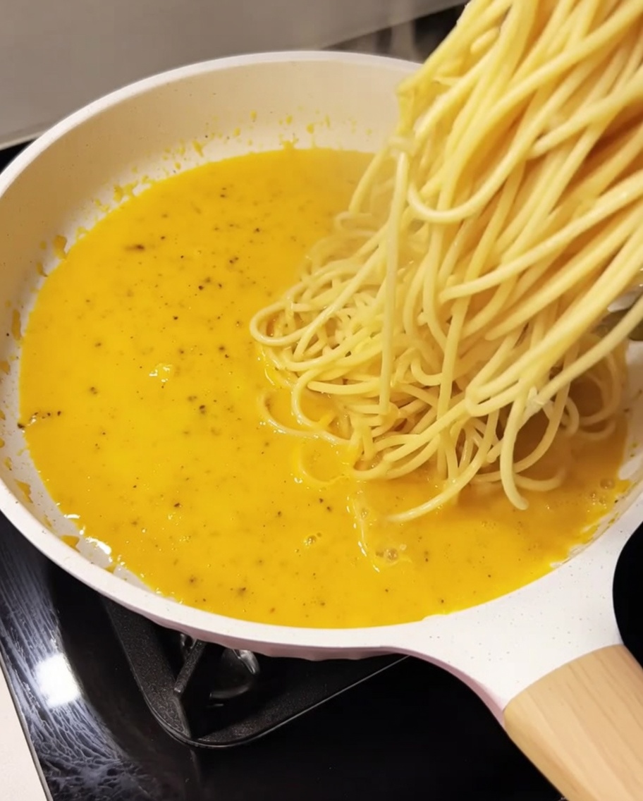 茹で上がったスパゲッティをソースの入ったフライパンに入れる様子。
