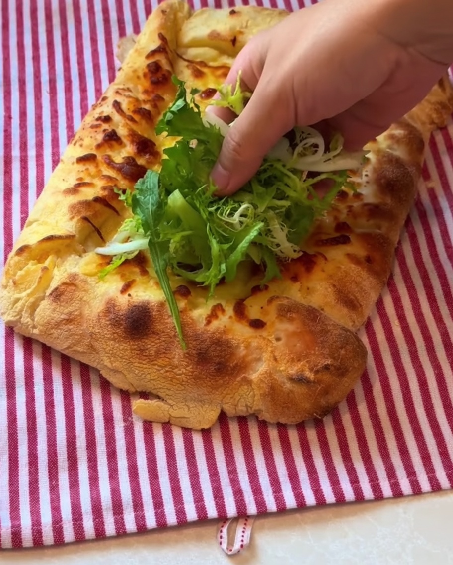 焼き上がったピザの上に、新鮮な野菜と生ハムをのせている様子。